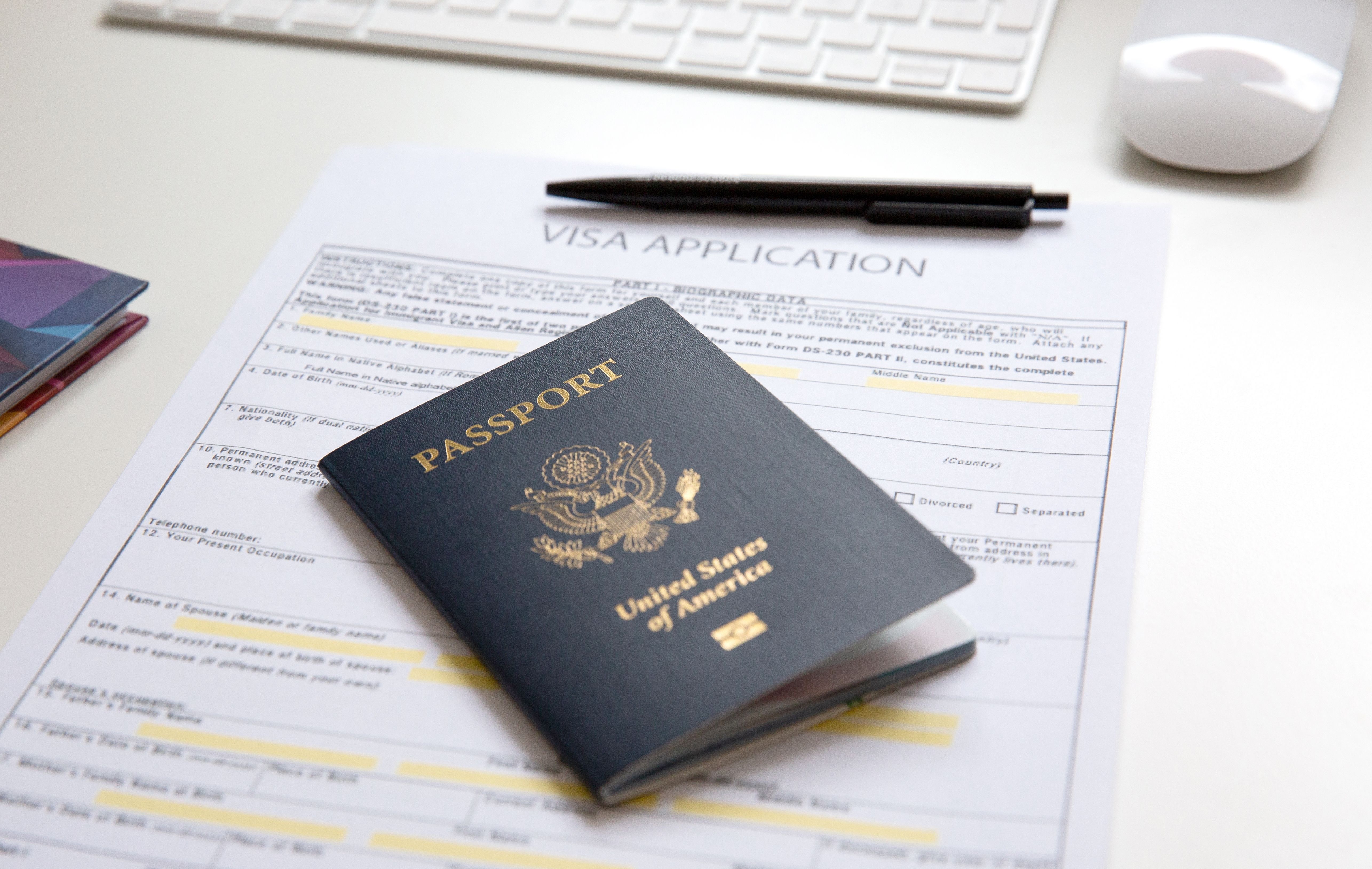 American passport with visa application documents, black pen and computer on white table