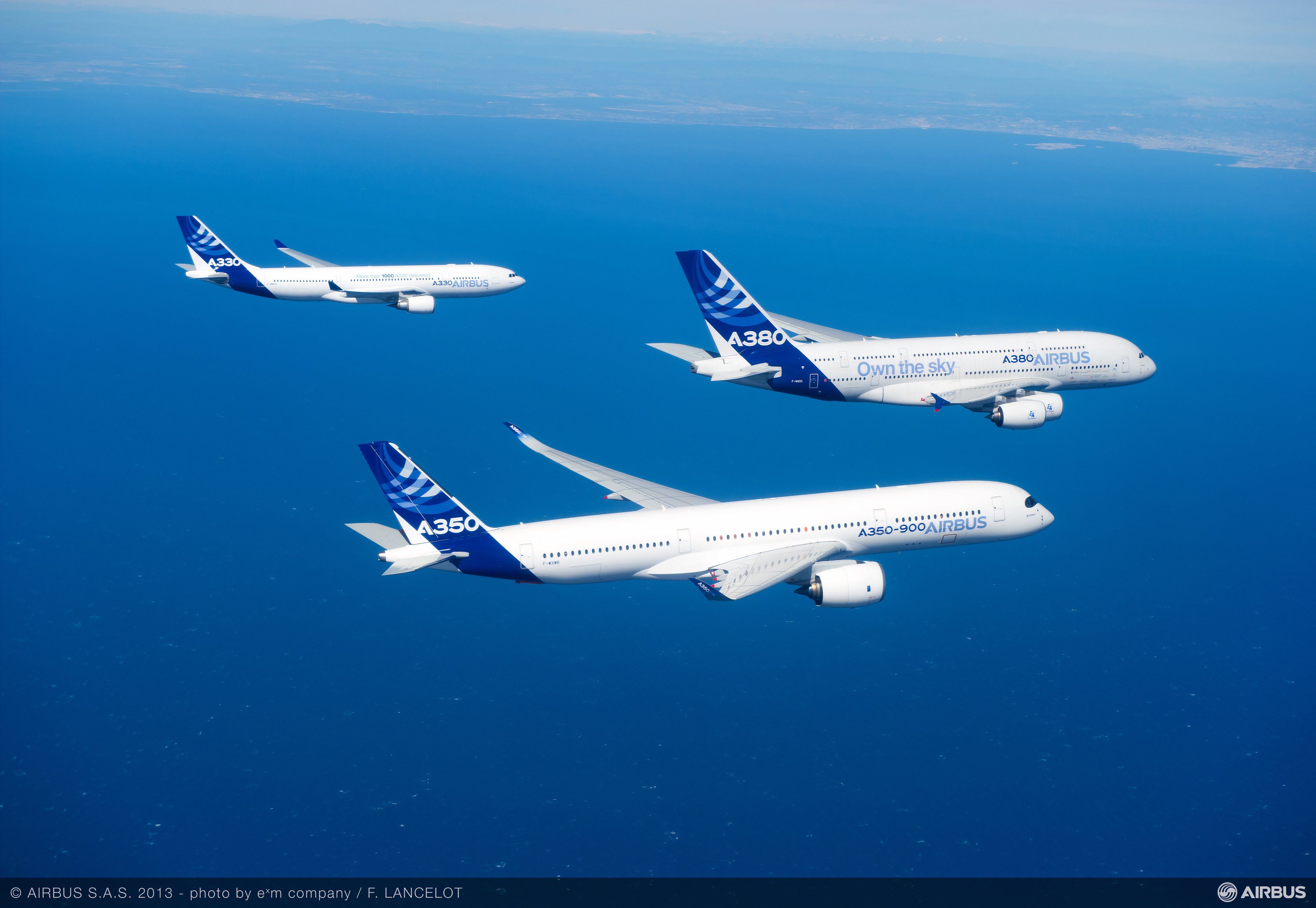 Three Airbus passenger liners flying together over the water.