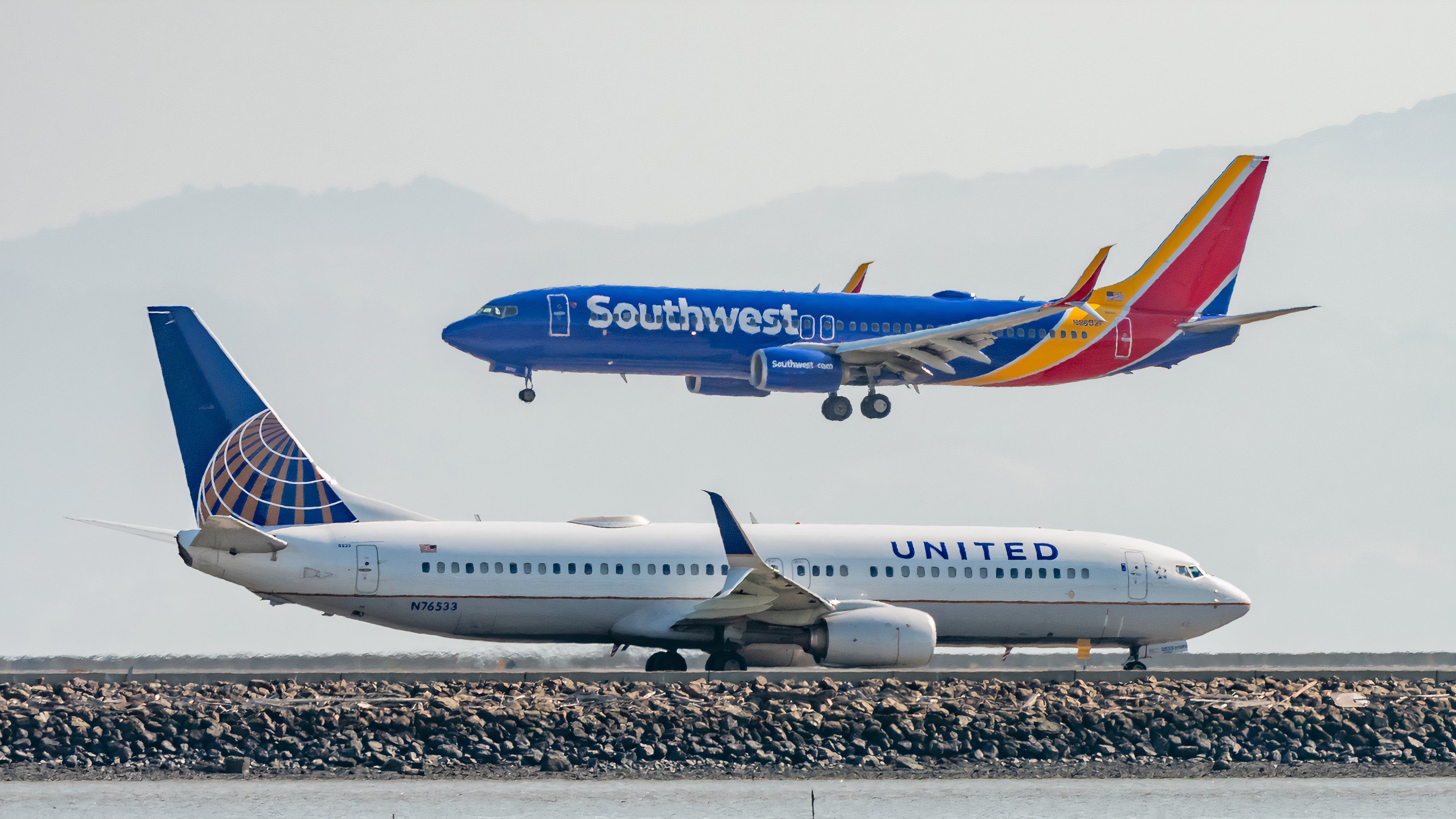 A Southwest Airlines plane comes into land as a United Airlines plane taxiis towards the end of the runway at San Francisco Airport.