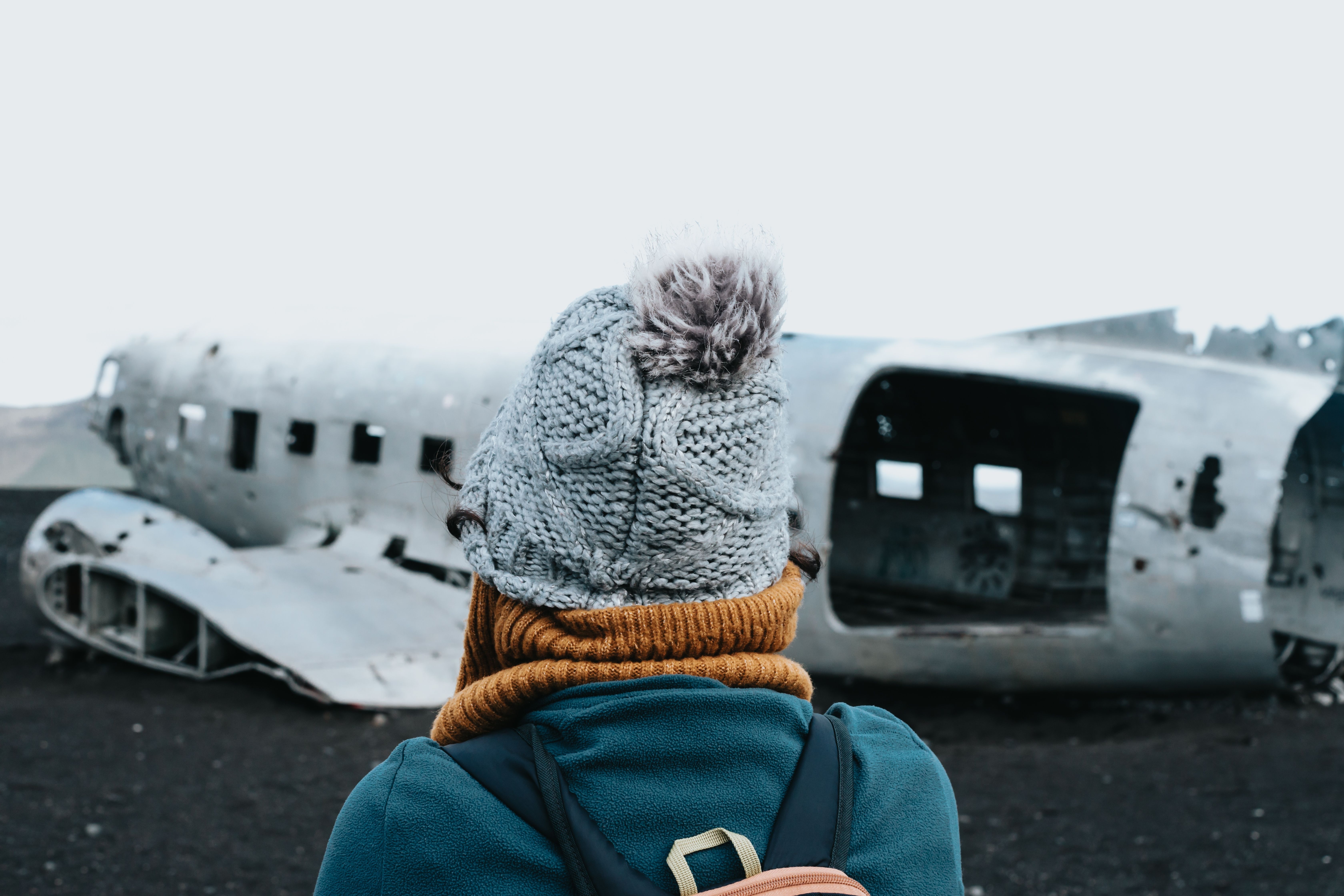 Woman in winter clothes in front of the wreck of the crashed airplane in Iceland, on the beach of Sólheimasandur.