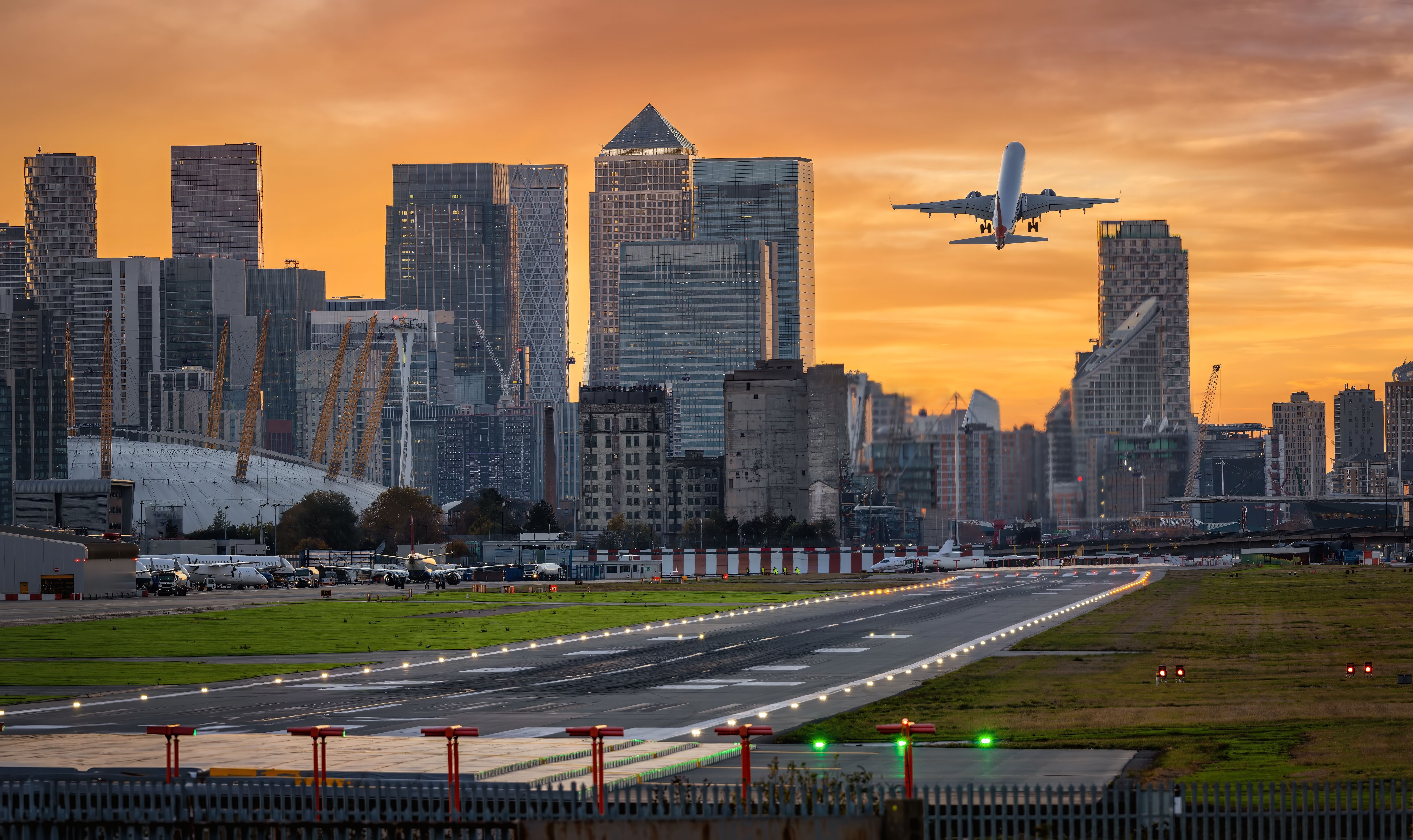 Panoramic view of the London skyline with the Canary Wharf district and the City Airport runway in front of it at sunset