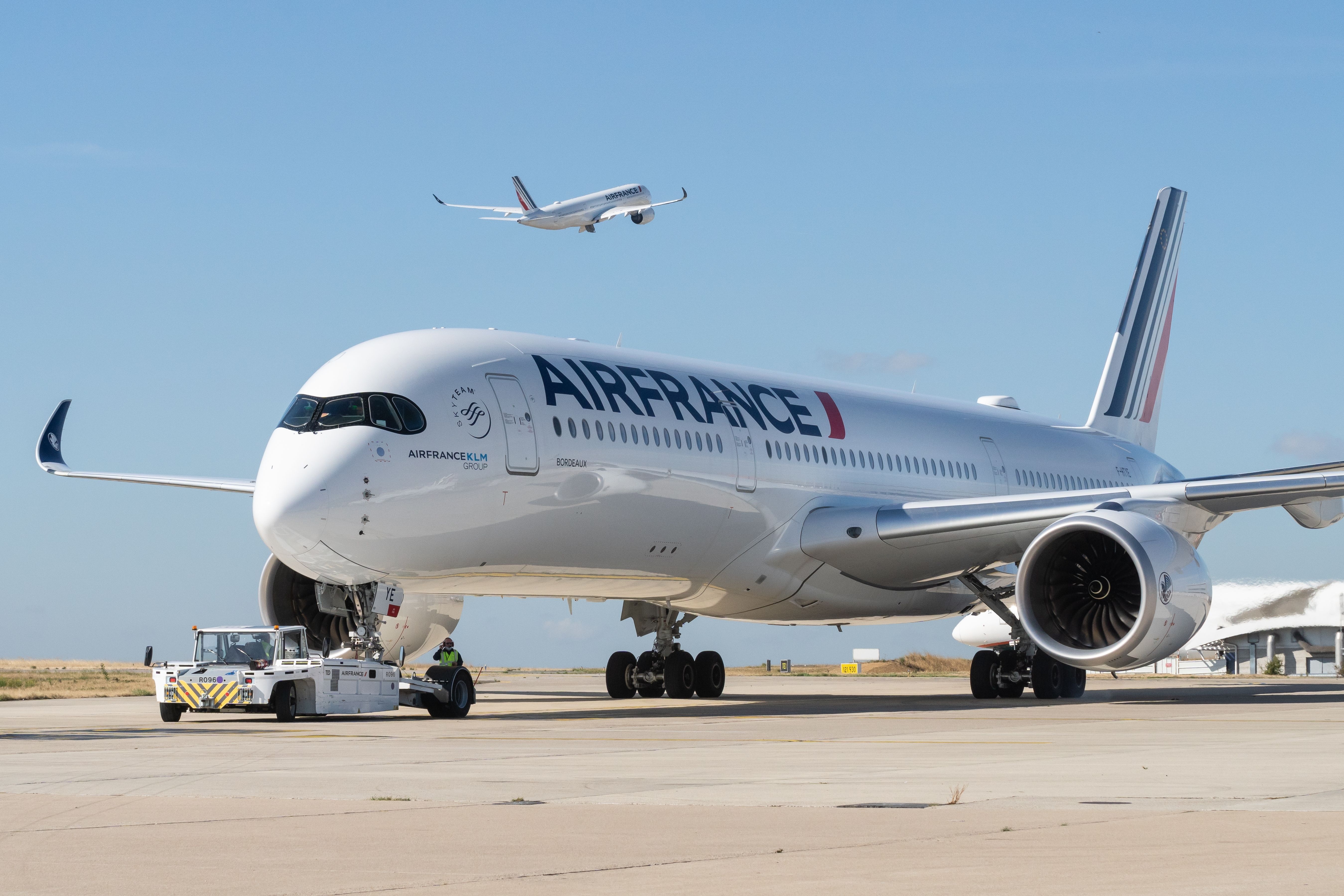 An Air France Airbus A350 on pushback while another A350 is taking off in the sky