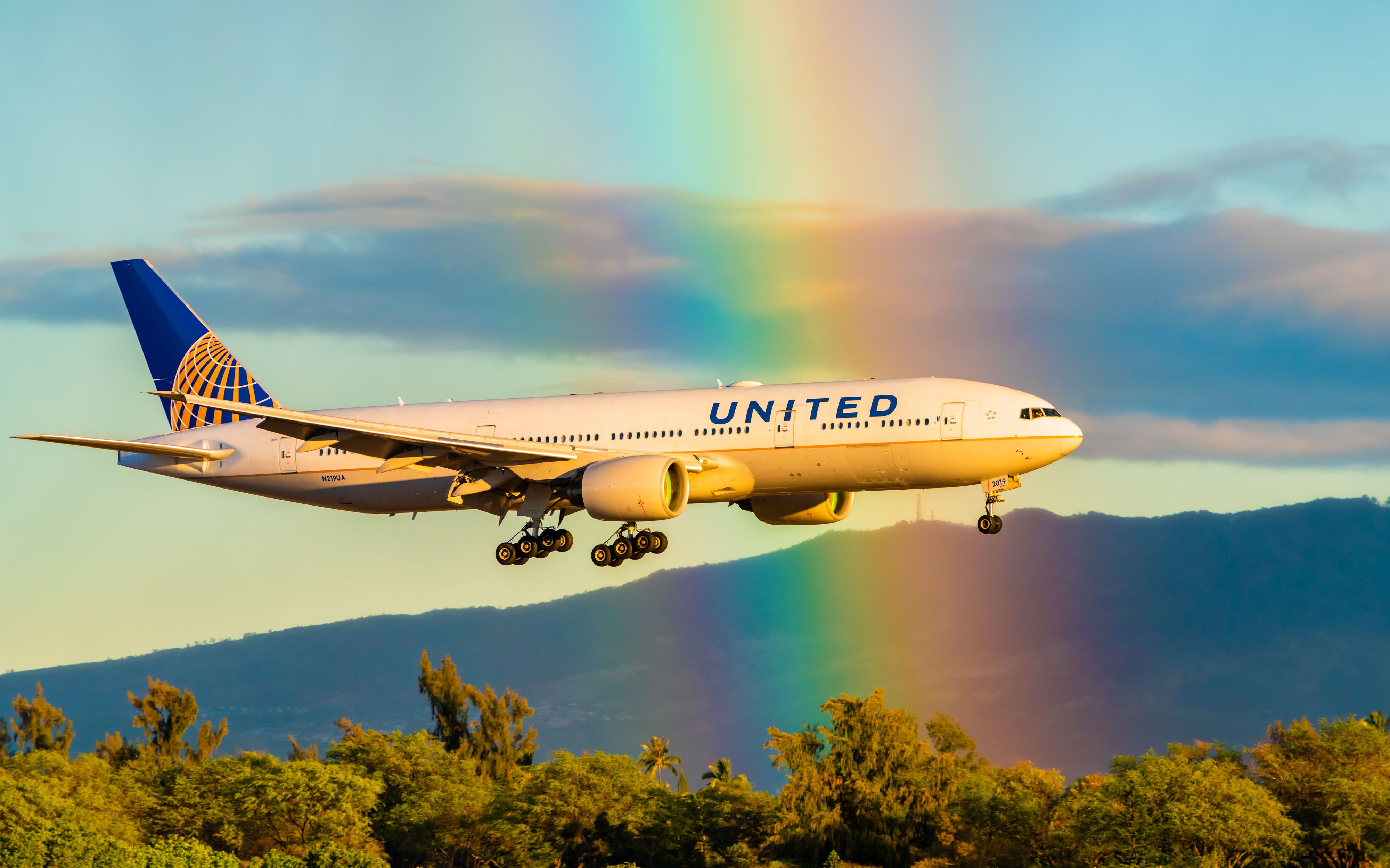 United Airlines Boeing 777-222 ER Registered N219UA flying through a rainbow PC shutterstock_1397936222