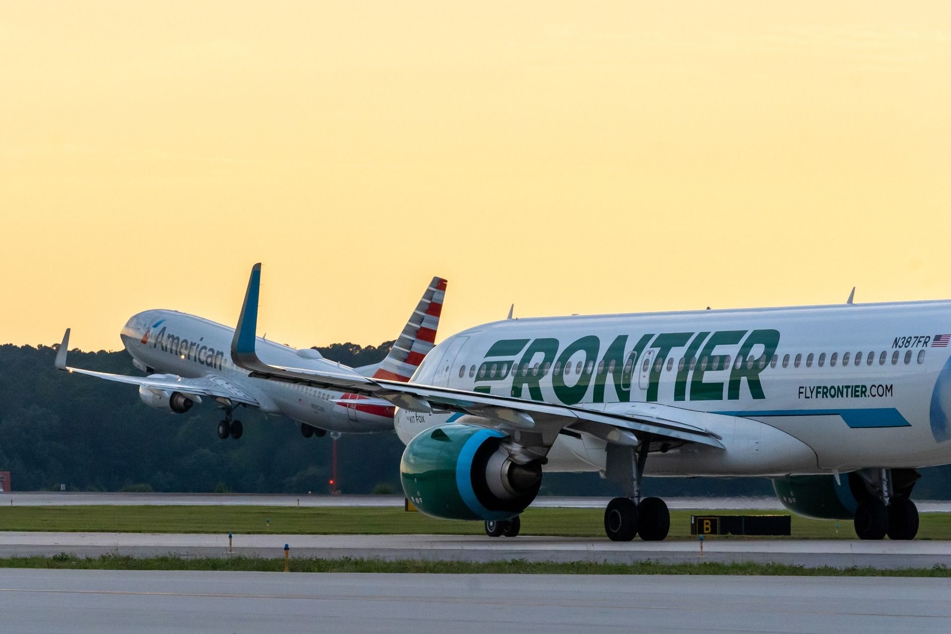 Frontier Airlines Airbus A320neo with American Airlines Boeing 737-823 taking off in the background at Raleigh-Durham International Airport.