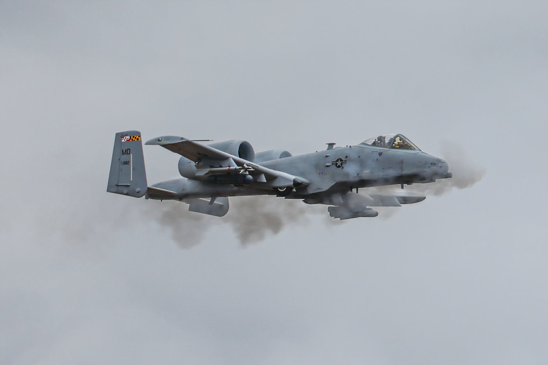 A-10 flying against a grey cloudy background firing its rotary cannon.