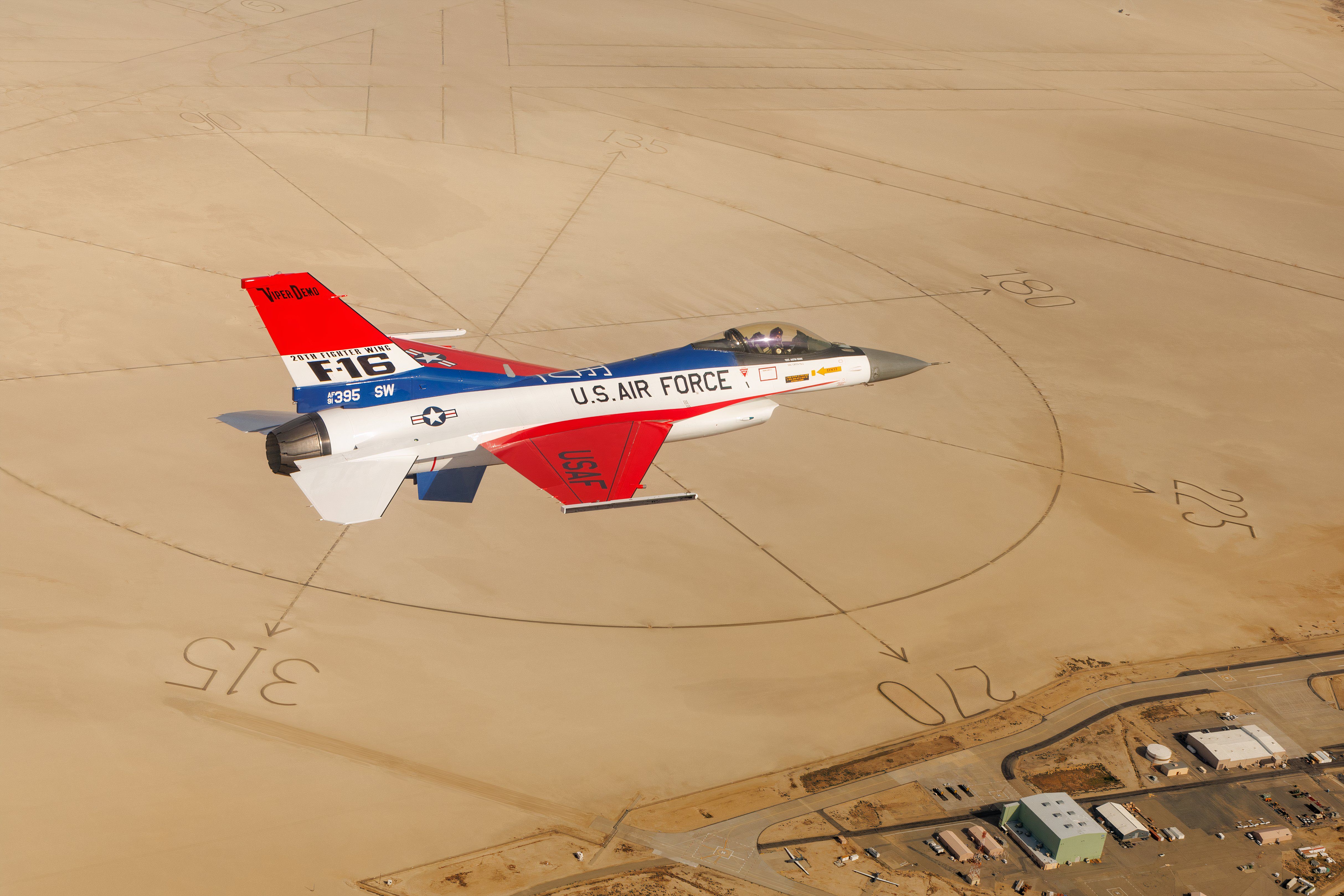 F-16 with red, white and blue paint flying over a desert.