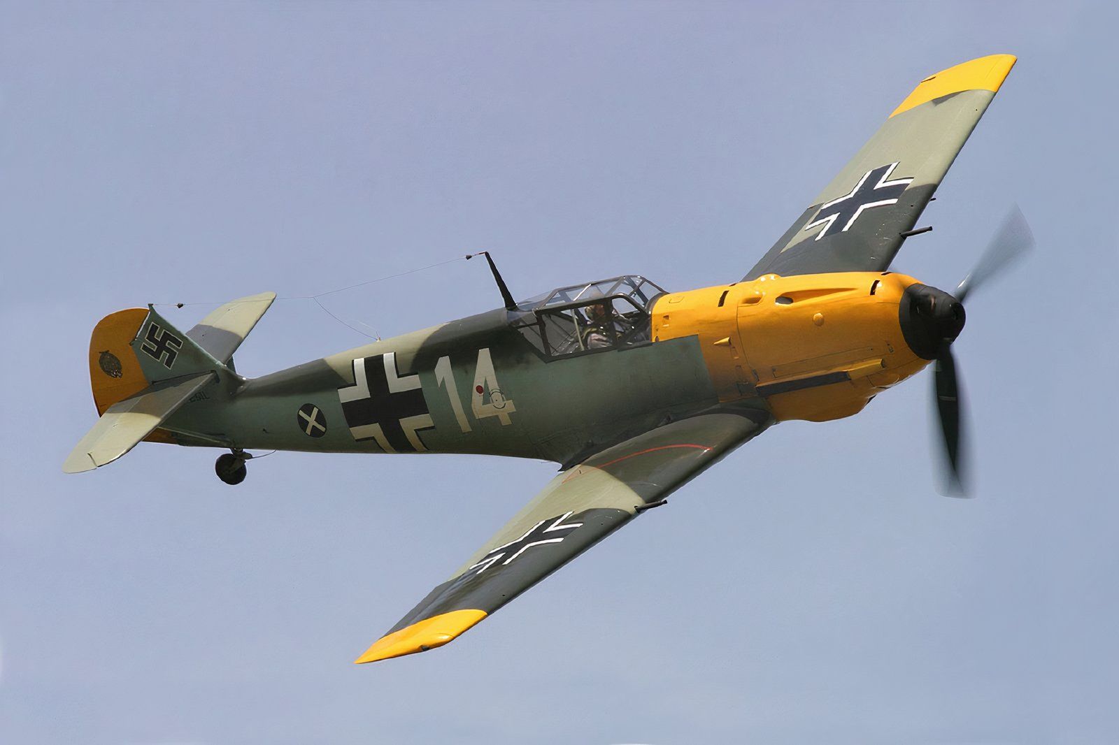 Messerschmitt Bf-109E flying against a light blue sky.