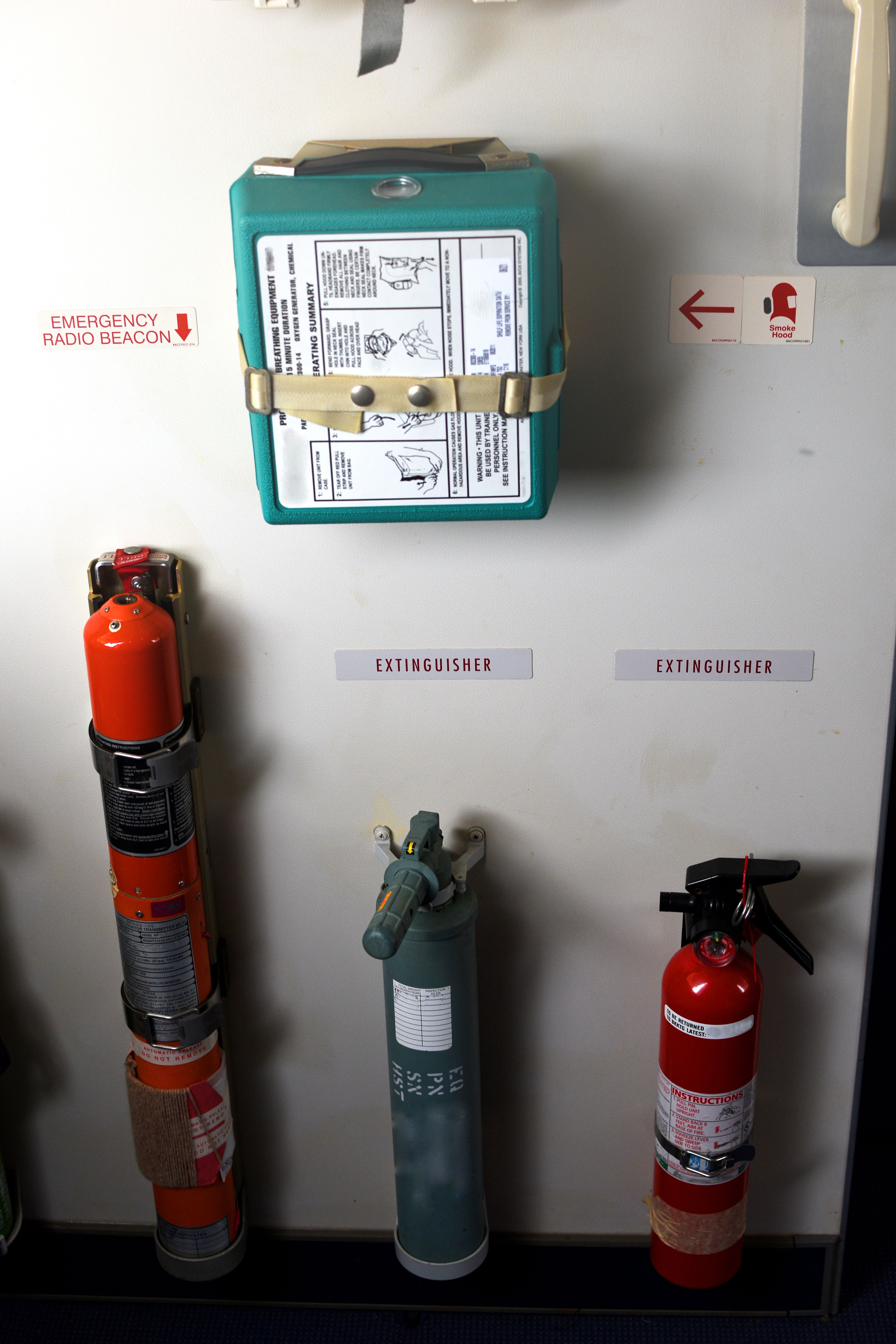 Photography of emergency equipment,extinguisher and first aid kit in aircraft (airplane) at exit door . Emergency radio beacon at aircraft (airplane) exit door.Two passenger seat in aircraft.