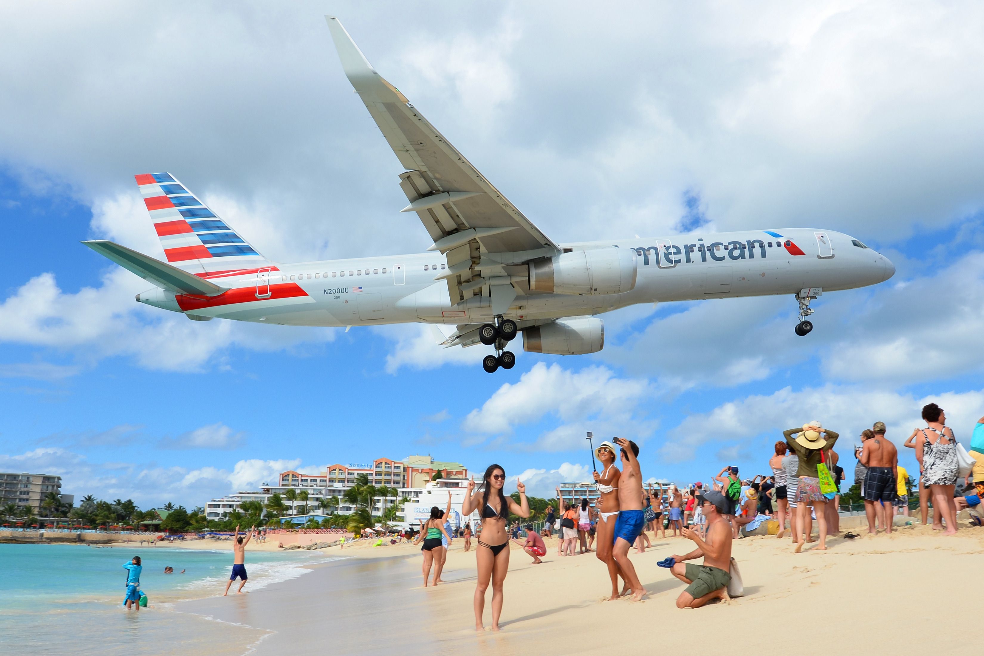 American Airlines Boeing 757 passing over Maho Beach with tourists posing for photos enjoying vacations. Airplane registered N200UU on final approach