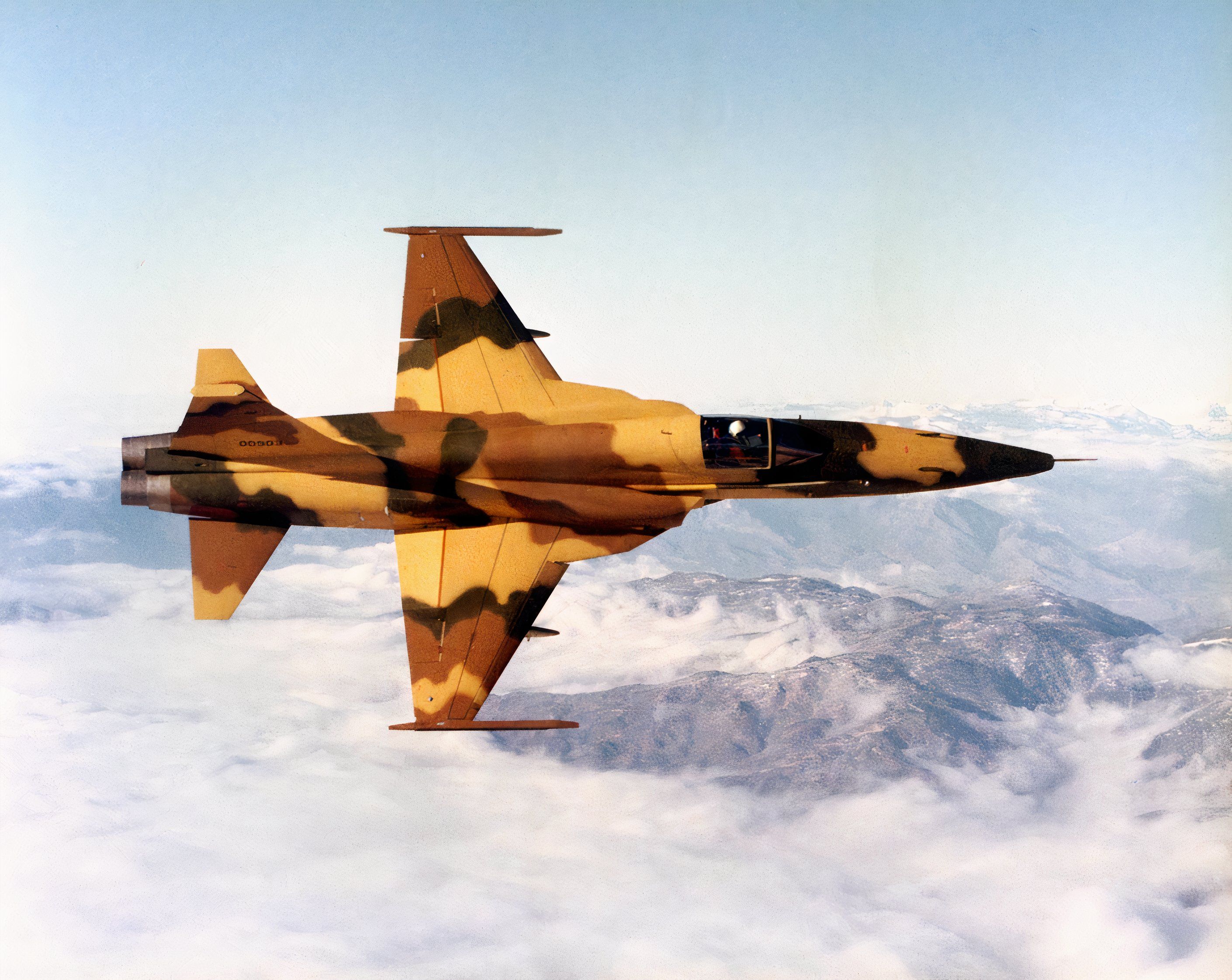 F-5 Tiger flying with a mountain range in the background.