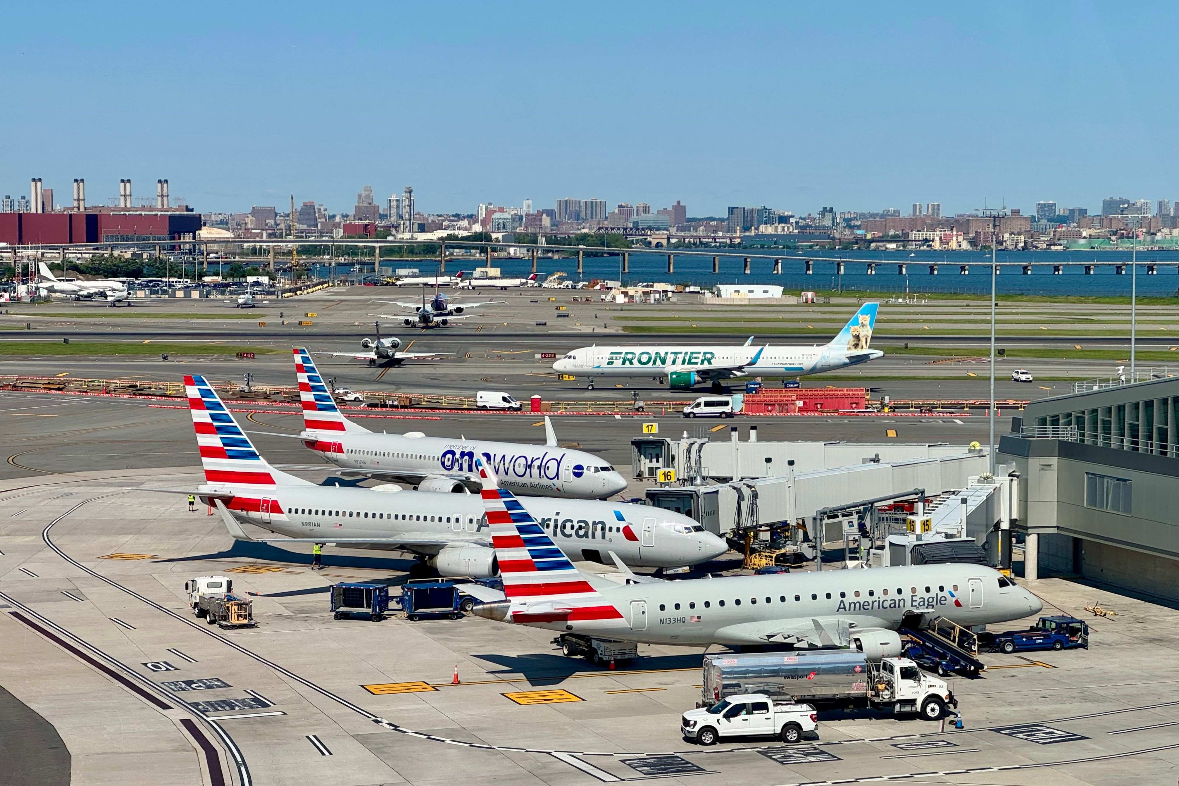 Airplanes line up to depart LaGuardia Airport LGA in New York City. American Airlines planes (including one in the oneworld Alliance livery) sit in the foreground as a Frontier Airlines plane rolls past