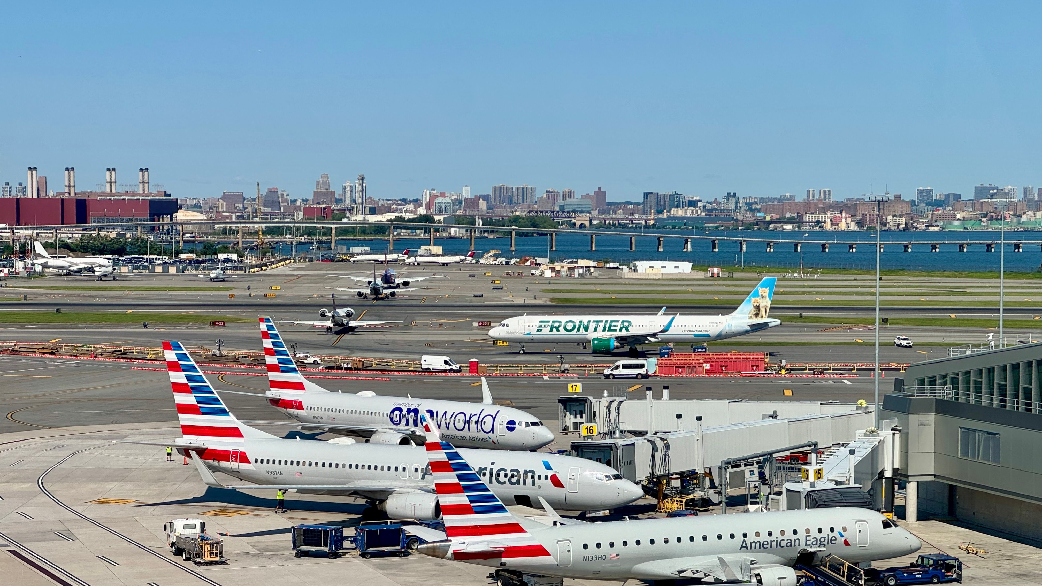 A Frontier Airlines plane joins the queue to take off from LaGuardia Airport LGA in New York City. In front American Airlines planes, including one in the oneworld Alliance livery, wait at the gate. 