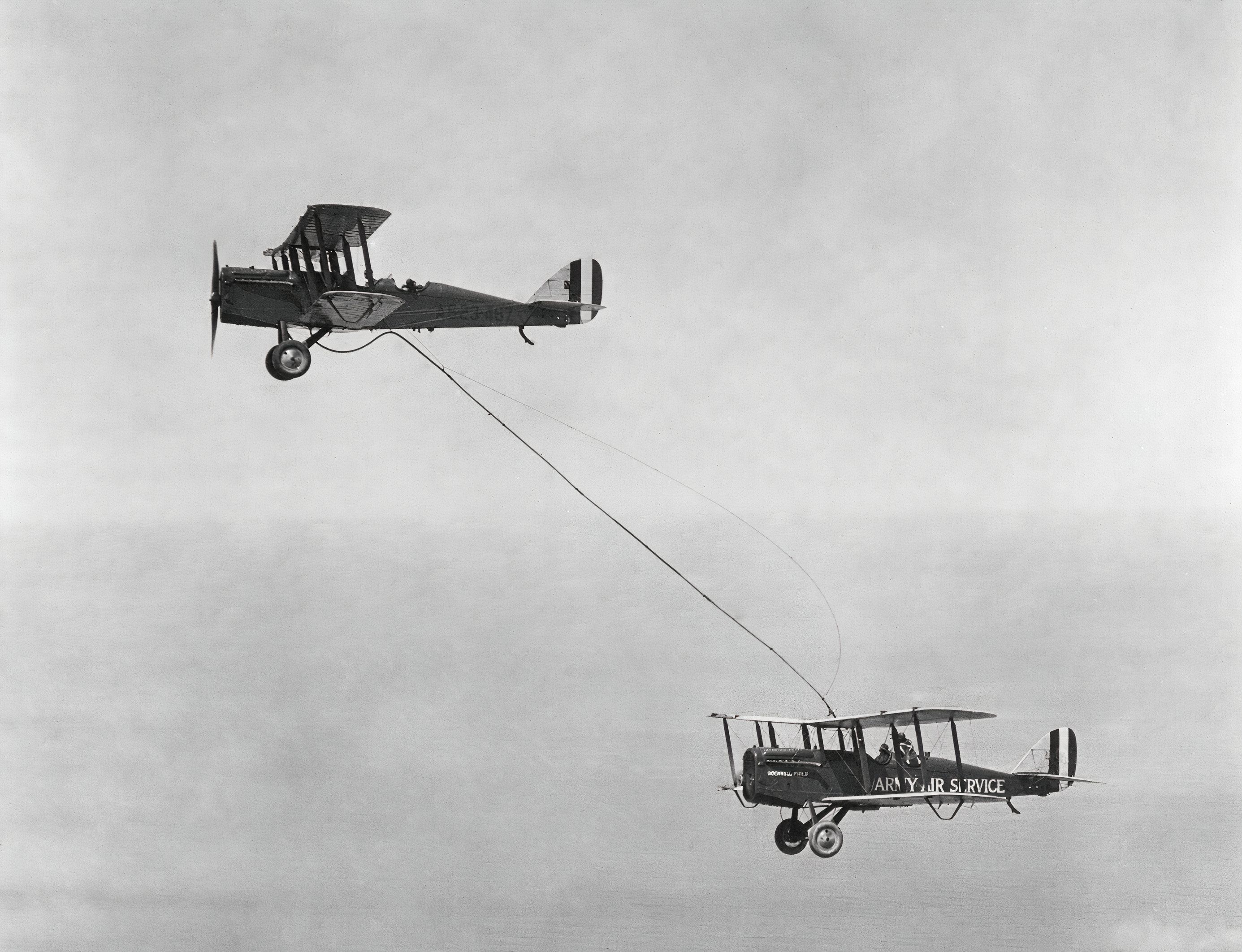 Black and white image of a biplane refueling another biplane