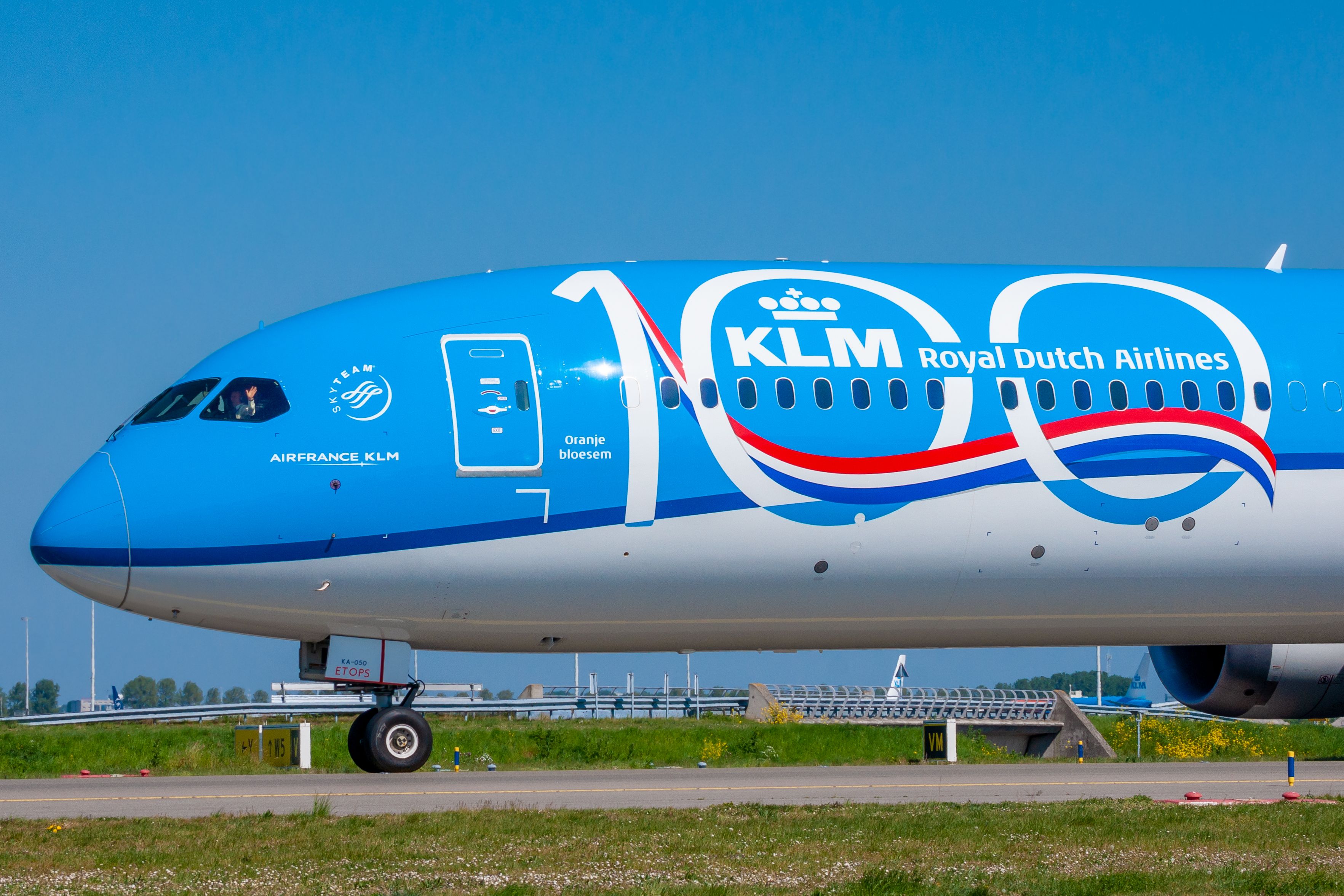 Waving pilot in KLM Boeing 787-10 with 100th anniversary emblem at Amsterdam Schiphol Airport