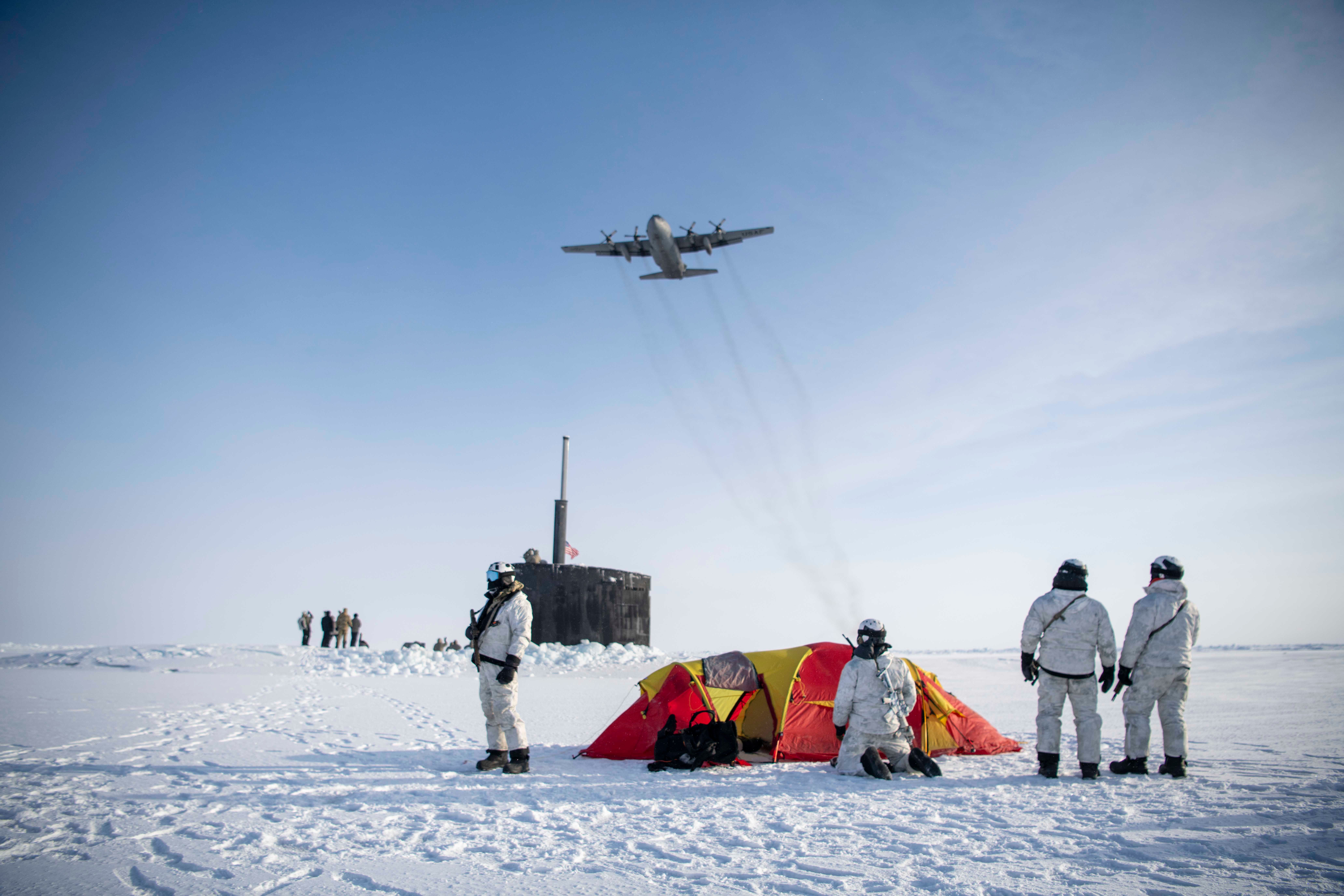 An Air Force C-130 Hercules flies over a group of Navy SEALs, Norwegian naval special operations commandos and the attack submarine USS Hampton during exercise Arctic Edge 