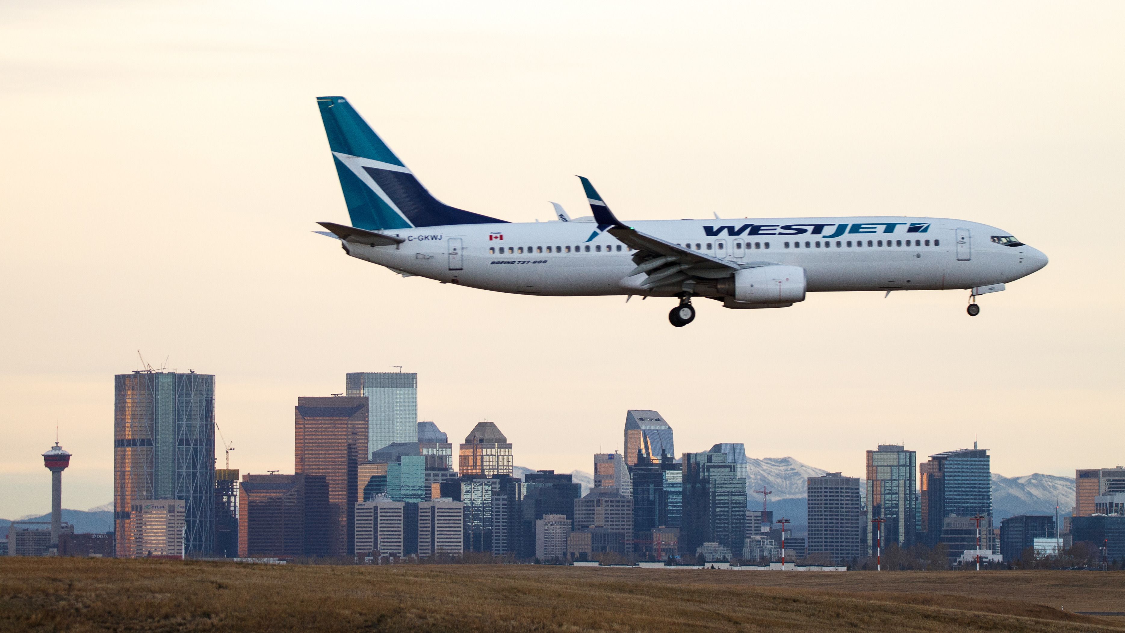 WestJet Airlines C-GKWJ Boeing 737-800 landing over the city skyline at Calgary International Airport.