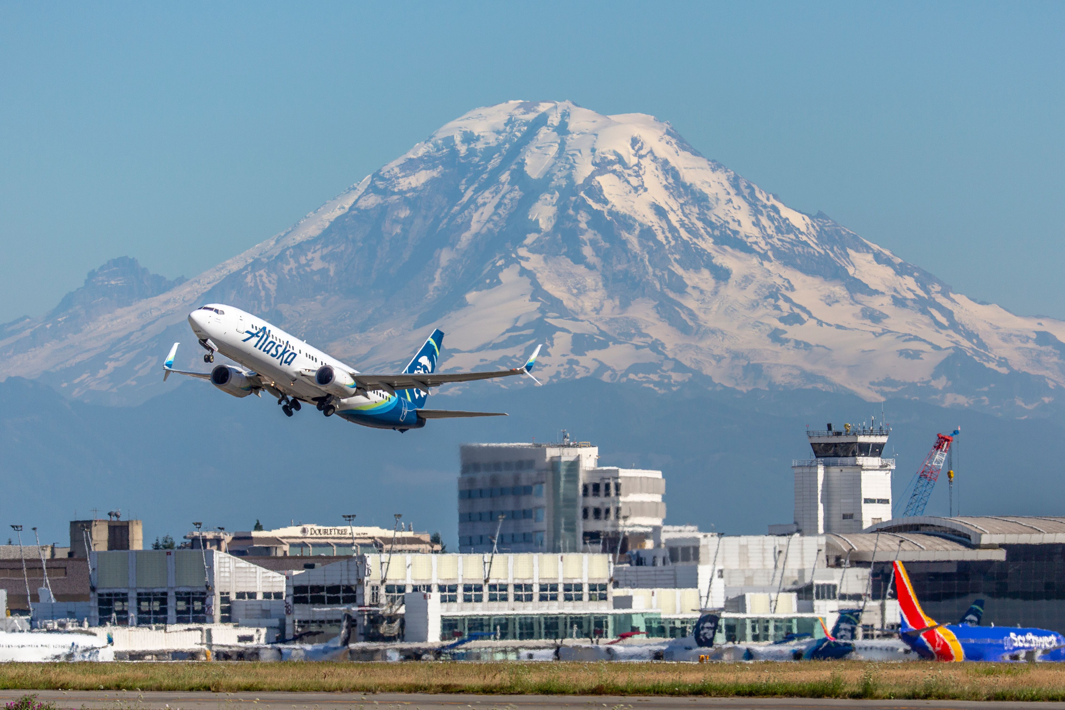 An Alaska Airlines plane at Seattle Tacoma International Airport in front of a Southwest Airlines plane and Mount Rainier