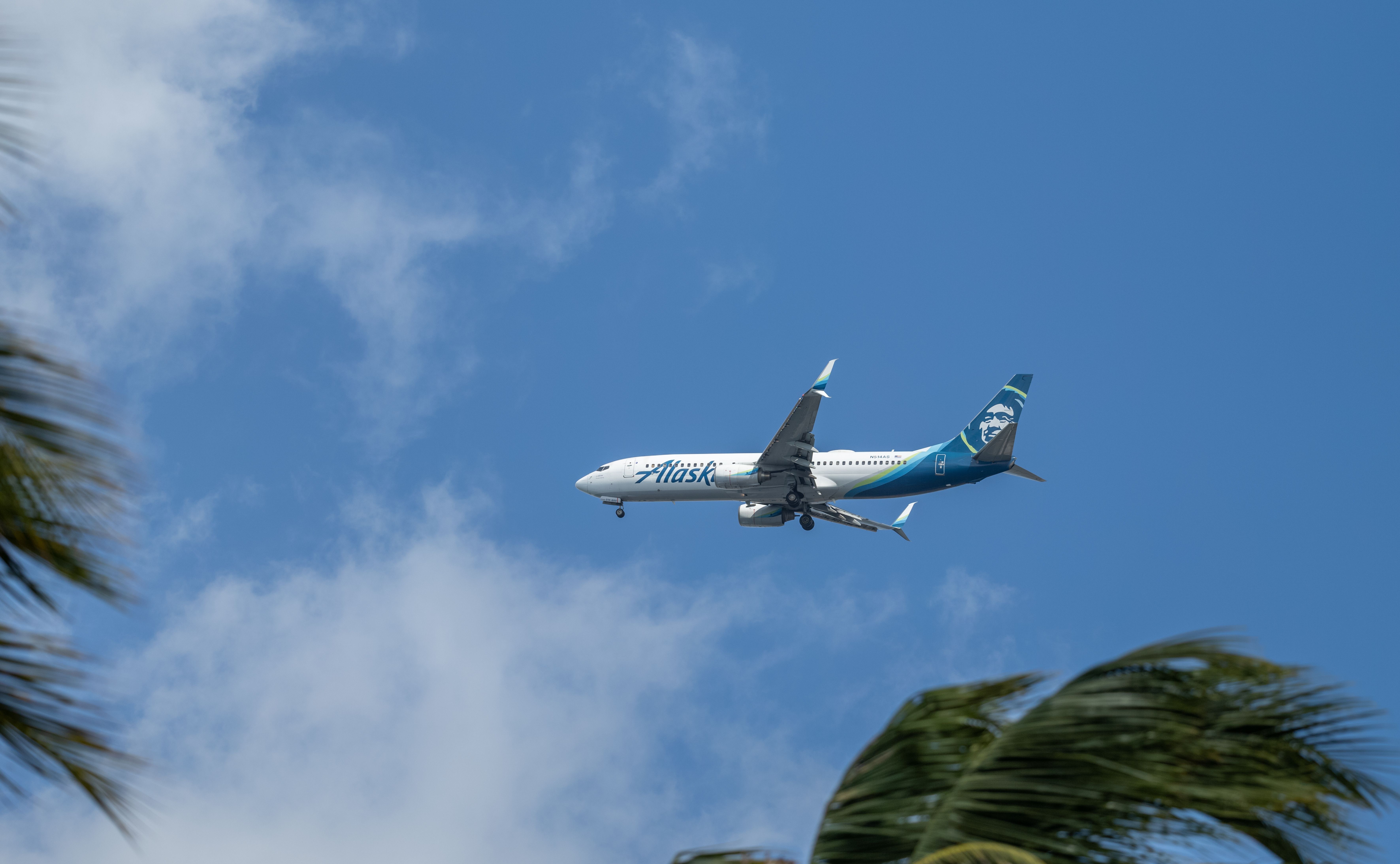 An Alaska Airlines Boeing 737 Max on approach to land at Honolulu Airport in gale force winds as palm trees bend in the wind.