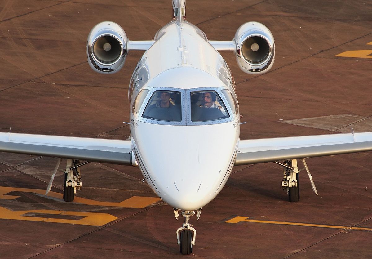 Phenom 100 on taxiway with pilots visible.