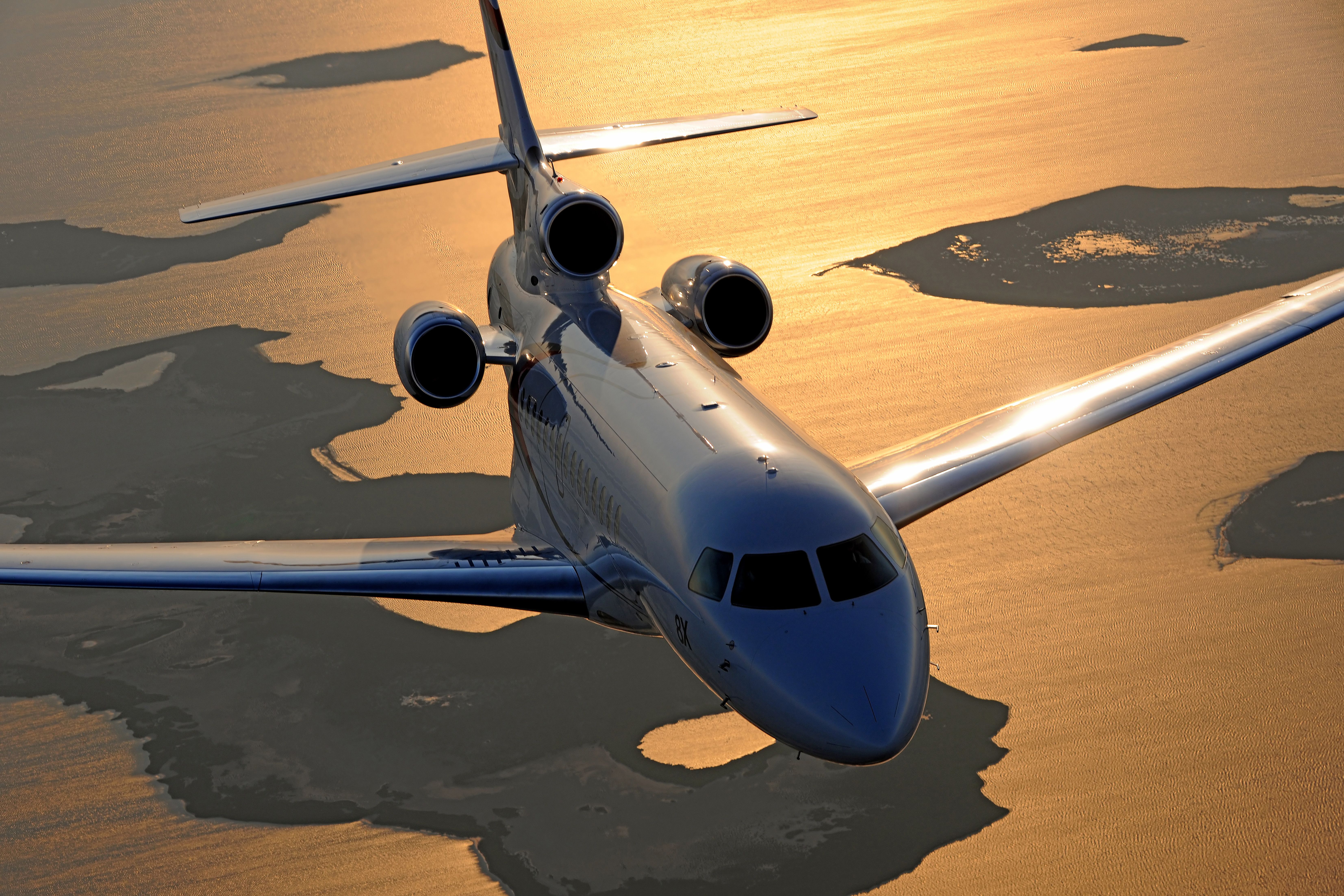 Falcon 8X flying over water at sunset.