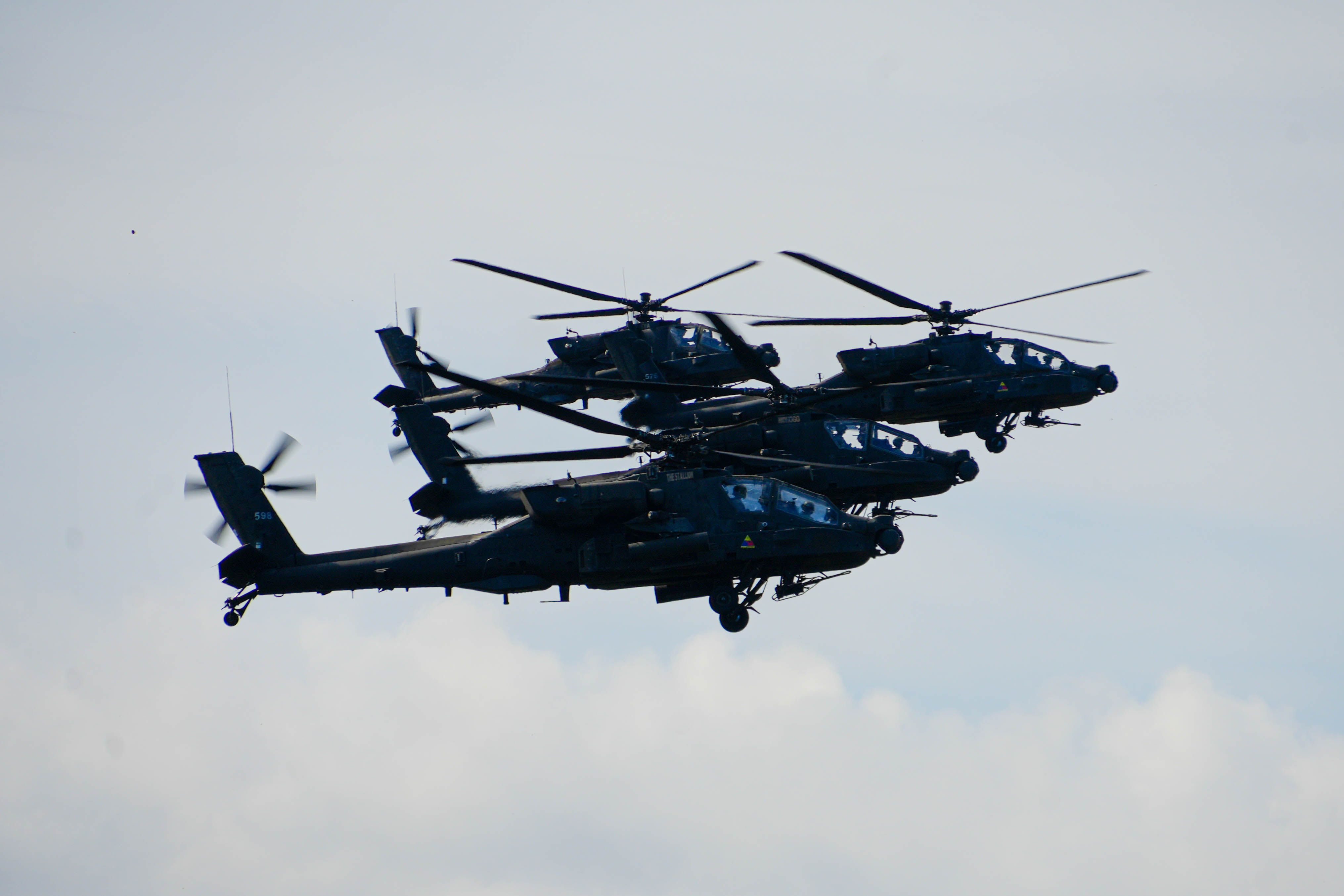Four U.S. AH-64 Apaches fly above the tree line during a training mission at Camp Ādaži, Latvi