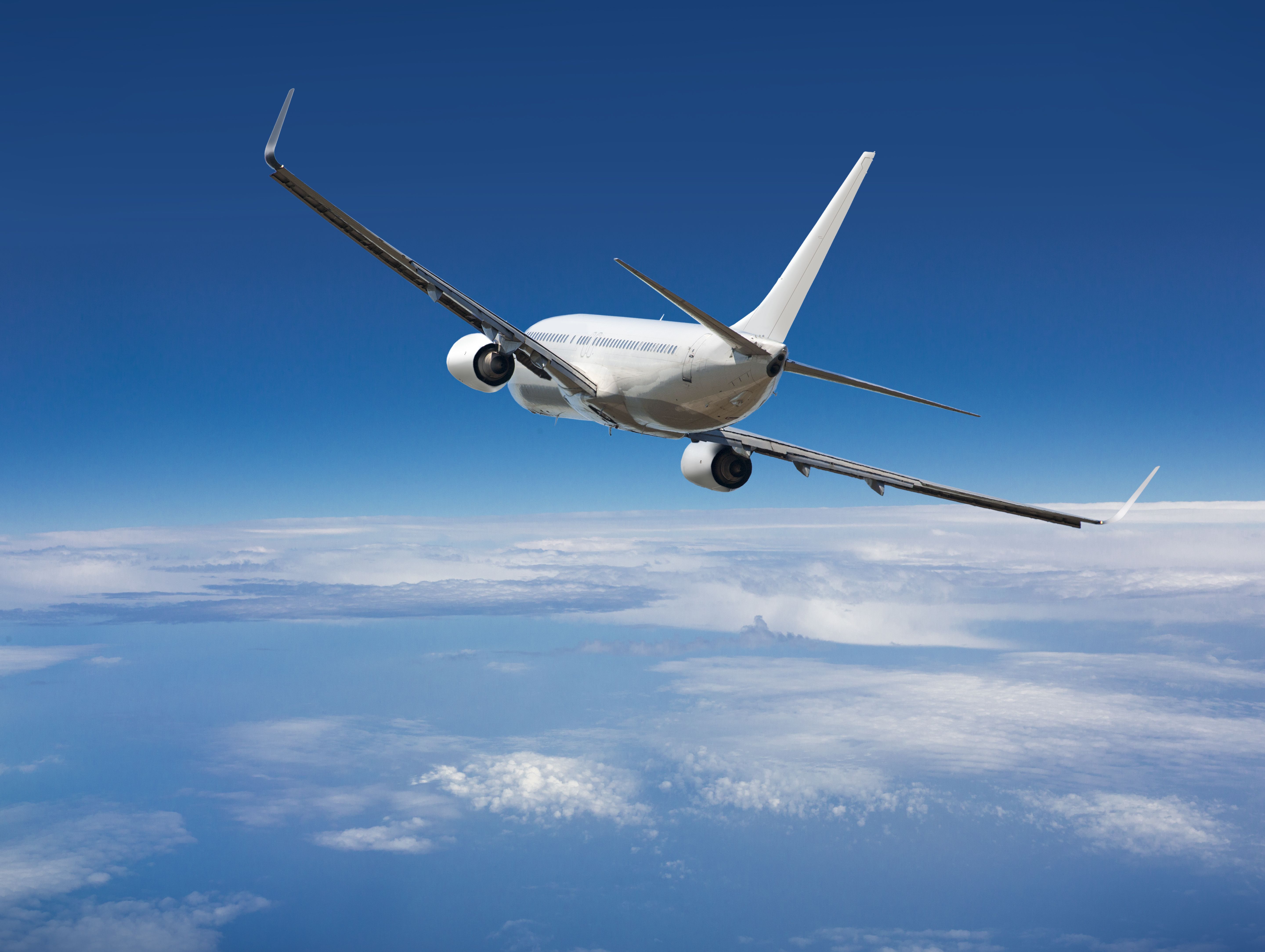 White passenger wide-body plane. Aircraft is flying in blue cloudy sky over the sea