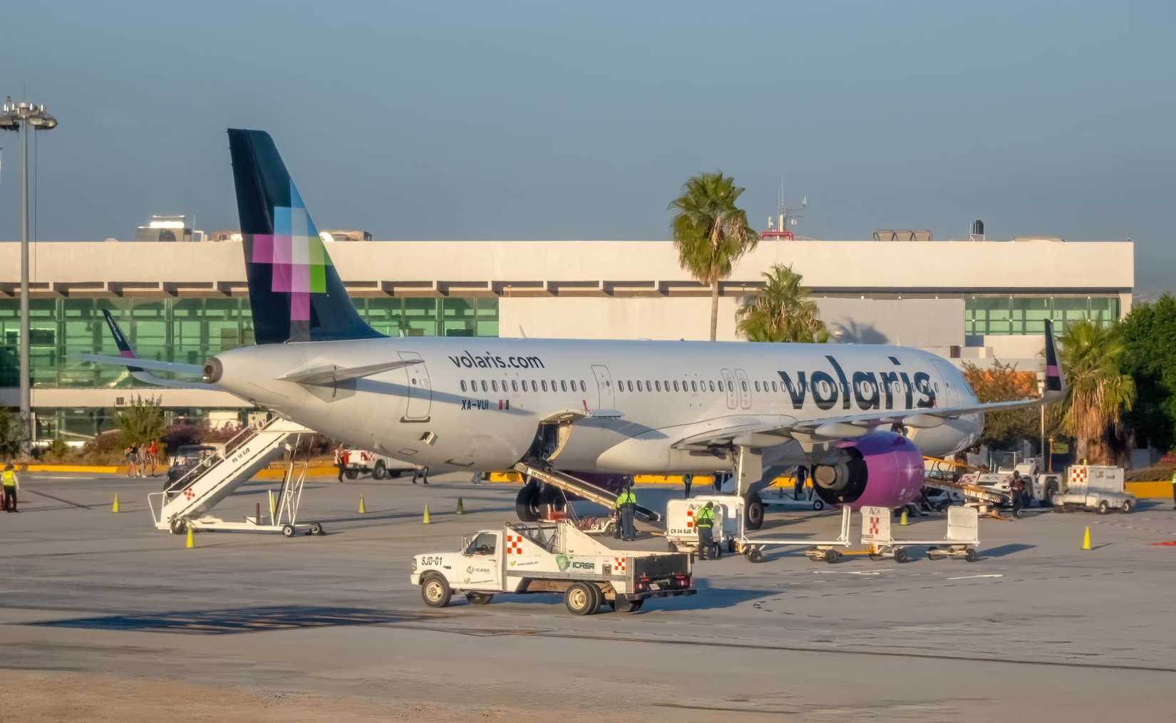 A Volaris Airbus A321 parked at an airport gate with ground crew preparing the aircraft for departure from the Los Cabos International Airport.