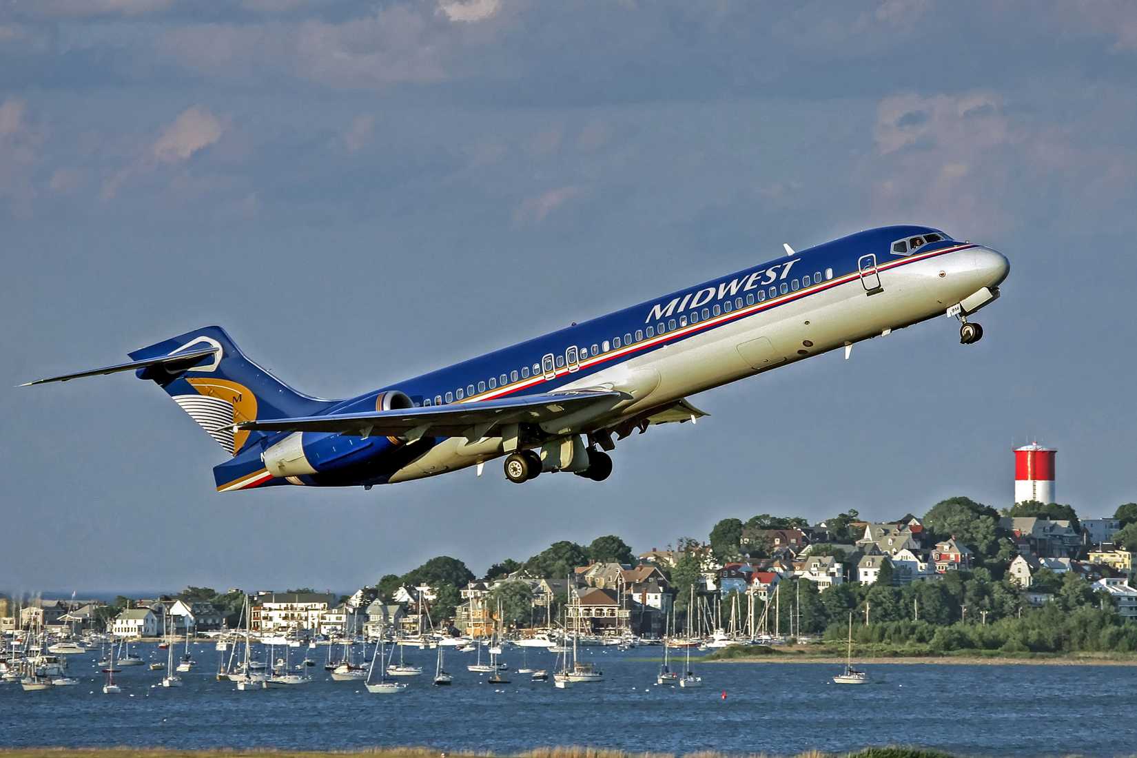 Midwest Airlines jet plane takes off from the runway and heads skyward, harbor background - Logan Airport Boston, Massachusetts USA - April 26, 2004